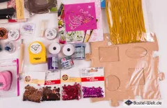 Detailausschnitt mit Holz-Schattenkasten, goldenem Bastelband und Pailletten in Braun, Rot und Pink.